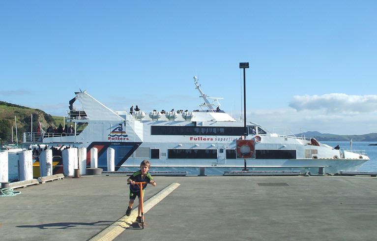 Jane Scorey; Boy on scooter and ferry; Fullers ferry leaving from Matiatia Wharf, Waiheke Island,