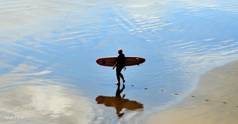 Picture of an elderly surfer heading for the surf. Picture taken from Muriwai beach