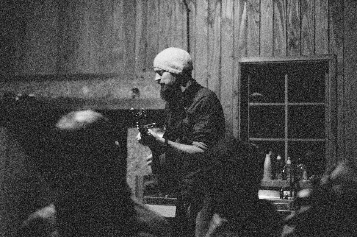 Scott Yeoman;Monty Bevins in Meadow Hut;At this particular moment, high on the Pisa Range, more than a thousand metres above sea level, there are only two sources of sound. There is the fireplace and there is the man in the light. His voice is raw, stripped back. There is no static or feedback coming from a microphone or amp because there is no microphone or amp. There is no electricity. No cell phone coverage. No distractions. Just a single bulb powered by the sun, a guitar, and a man singing his first song of the night.