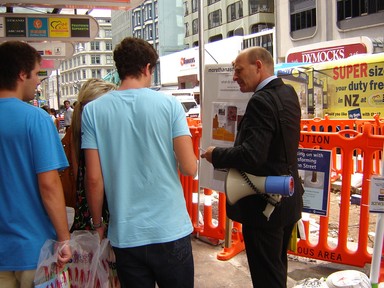 Untitled; A man tries to explain the Rugby World Cup stadium is in the wrong part of town! He engages people on the street with his mobile placard