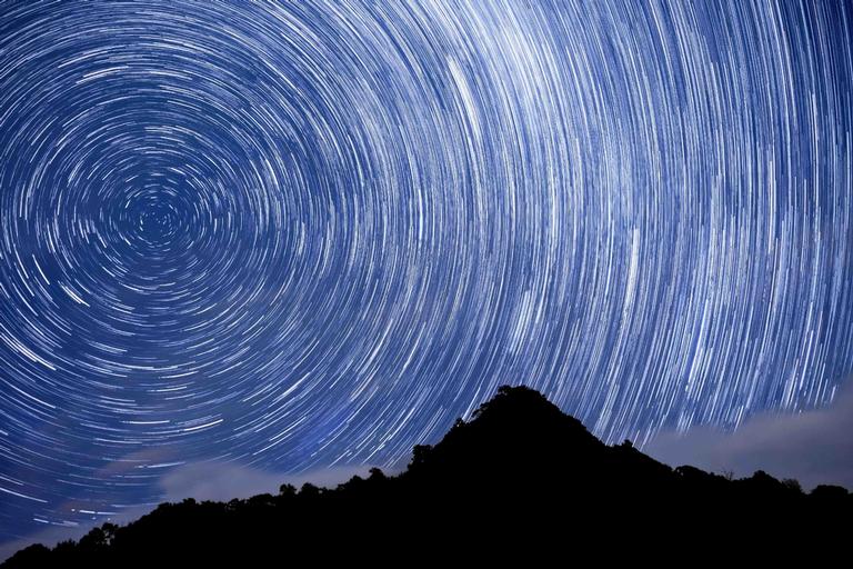 Mirjam van Sabben;Te Komoki Ancient Pa Under Ancient Stars;This photo was taken on the 9th of June 2018 at Little Huia. Many driving through this tiny seaside village on their way to Whatipu Beach are unaware of the rich history of this beautiful landmark. Te Komoki, known by locals as Jacky’s Peak, is one of the best preserved pa sites in the Waitakere Ranges, used in the past by Te Kawerau a Maki tribe inhabiting the area. Both this pa and the light of the stars by the time we see them are ancient. They are of the past, and yet seen and even preserved, by my camera in the present. This notion of preserving history has always fascinated me, as has astronomy. To combine the two in a single one hour long exposure was a great joy. The view is of the constellation Carina, and includes within it a large nebula and several open star clusters as they circled around the Southern Cross. The turquoise colour seen above the cloud on the left of the cone is a Large Magellanic Cloud, a dwarf galax