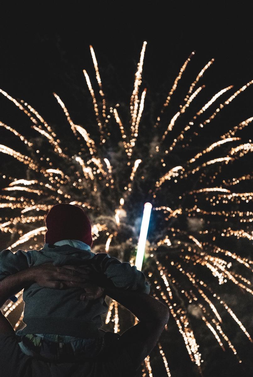 LEYAO LIU;A Father’s Love;A touching photo of a father holding his baby on his neck, as they watch the fireworks at the Hamilton hot balloon event. The photo captures the bond between the father and the child, as well as the joy of the festive occasion.