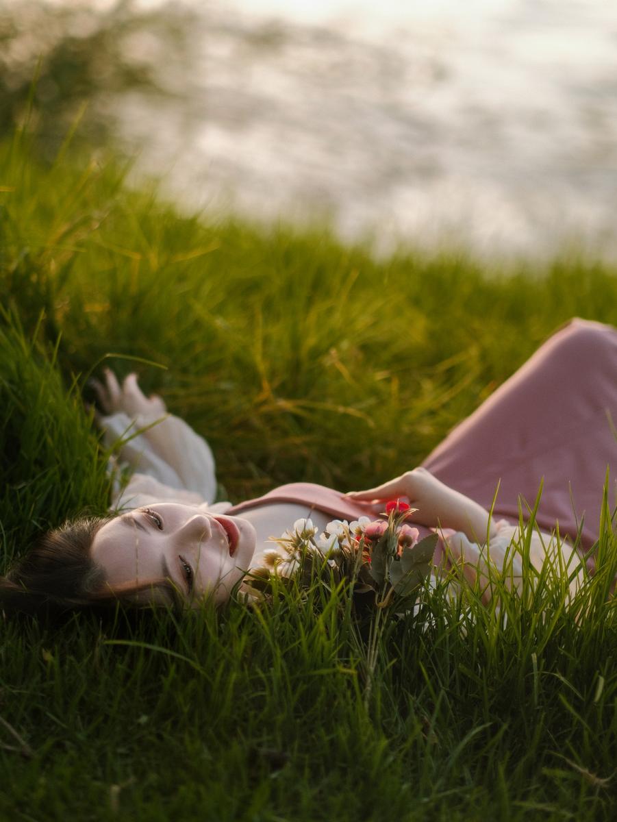 Jingjing Lyu;She Rests Where the Lake Breathes;In the hush of a summer afternoon, she lies where the earth meets water, eyes open to a sky stitched with dreams. The grass cradles her like a quiet secret, while the lake murmurs soft lullabies. In that stillness, youth takes root — tender, fleeting, and eternal.